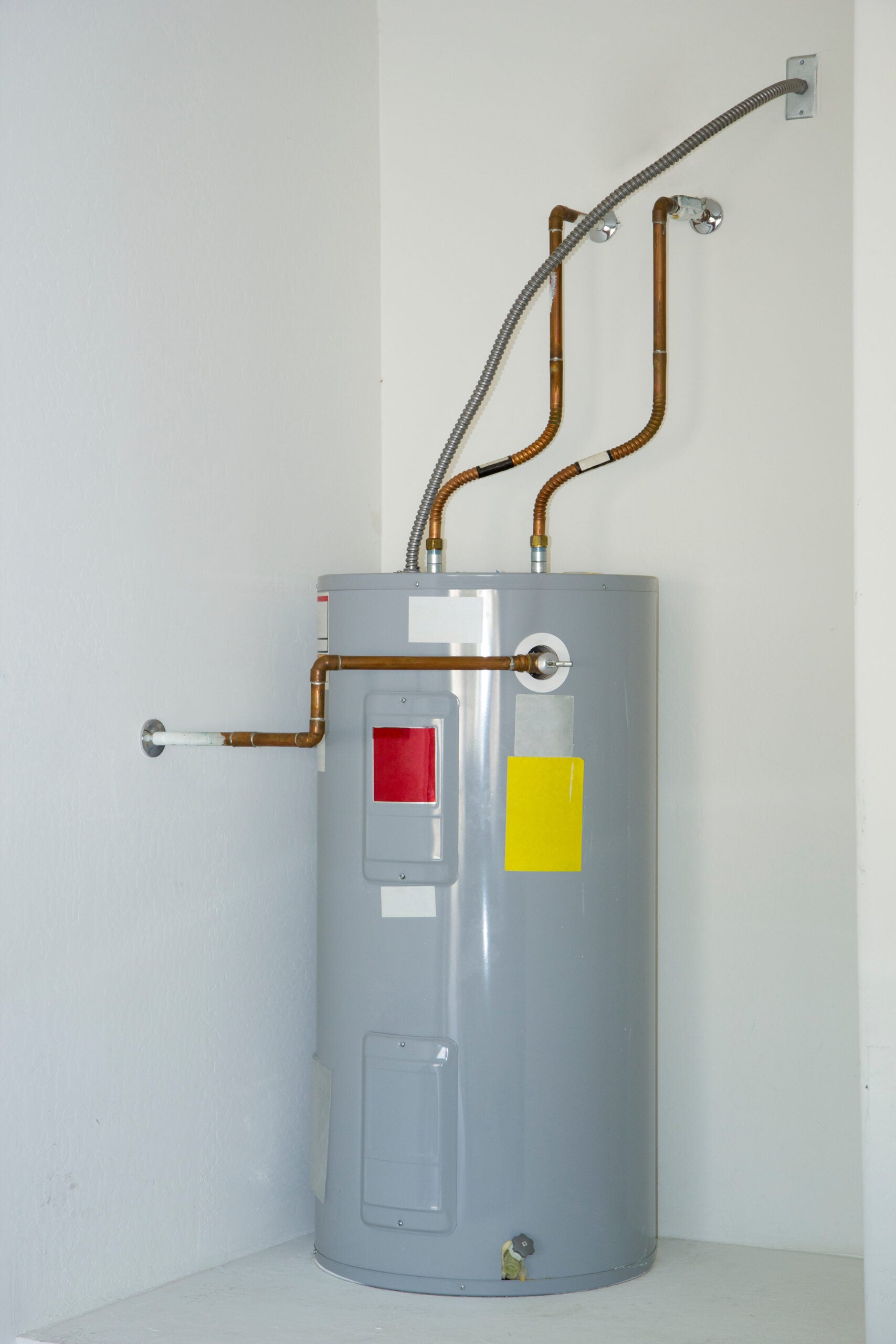 Grey cylindrical appliance with pipes connected to the walls in a white corner