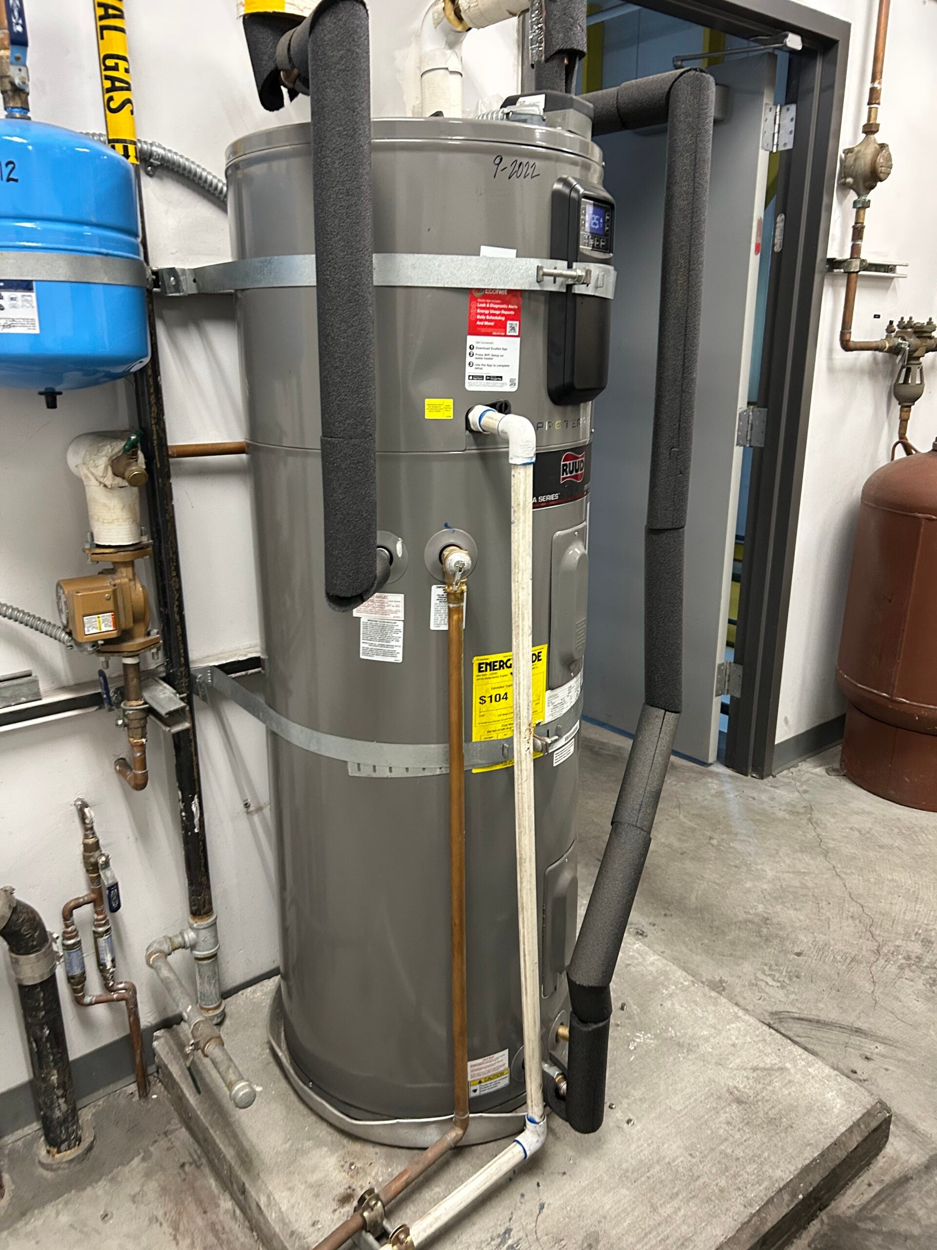 A tall, cylindrical gray heat pump water heater with a small electric screen and a vent near the top.